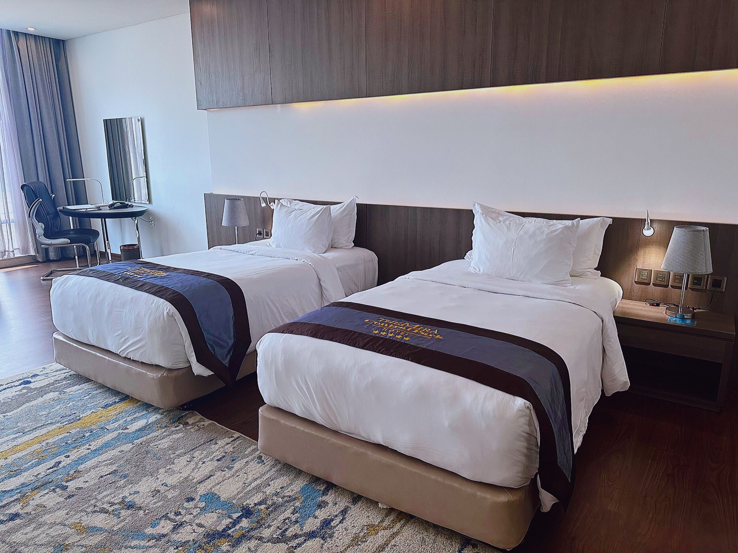 A hotel room with two beds, a desk, and a chair.