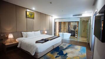 A modern hotel room with a large bed, bedside lamps, a bathroom with a glass shower enclosure, and a view of the interior.