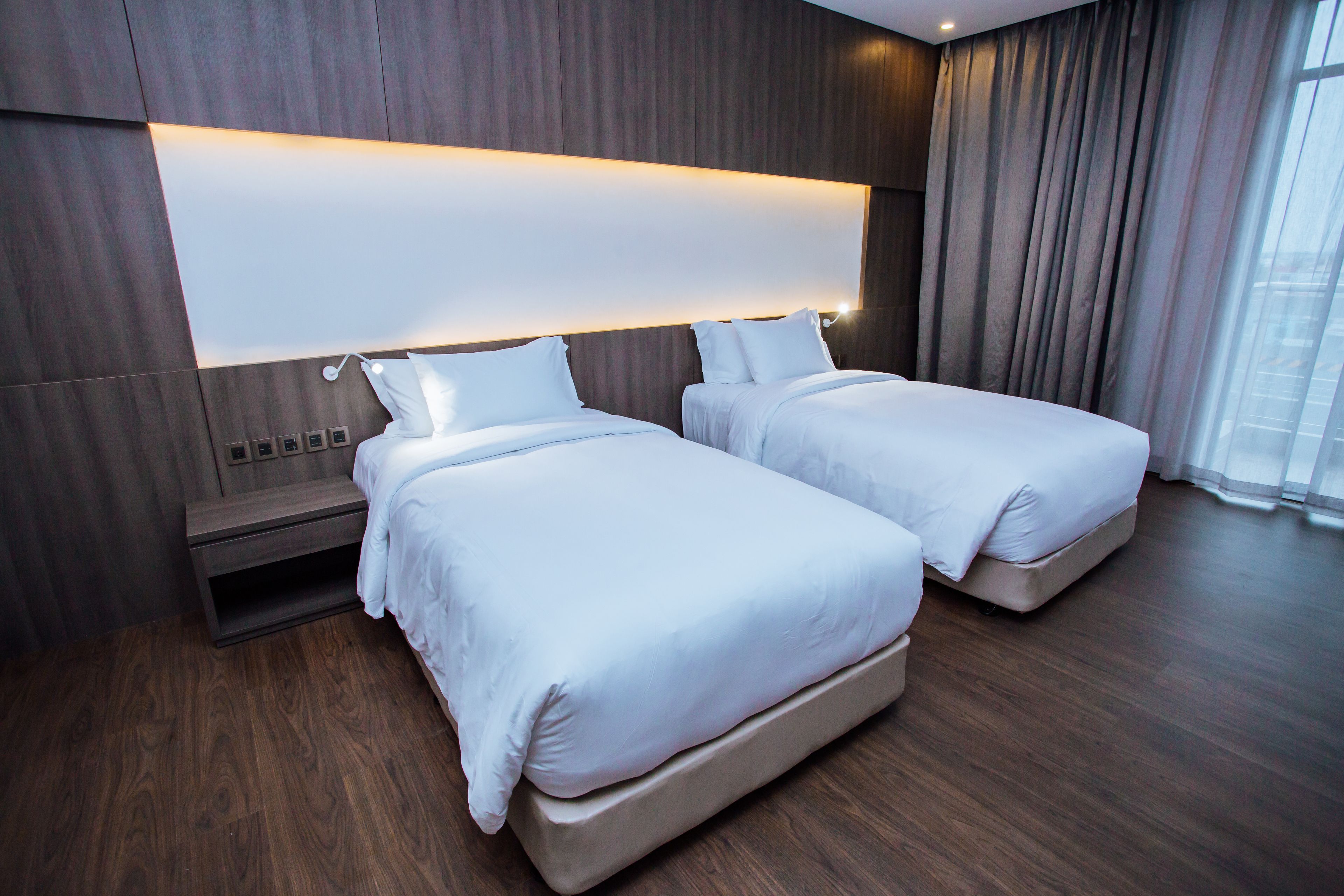 Une chambre d’hôtel moderne avec deux lits, un grand panneau lumineux au-dessus des lits et une vue sur la ville grâce à de grandes fenêtres.