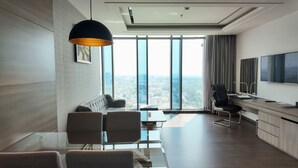 A modern hotel room with a dining area, a large window with a city view, a flat-screen TV, and a black pendant light. - The Mira Central Park Hotel (Bien Hoa)