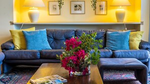 Ein Wohnzimmer mit einem dunkelblauen Sofa, bunten Kissen, einem Couchtisch mit Zeitschriften und zwei Wandlampen.