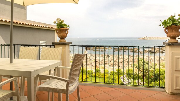 Eine Terrasse mit Tisch und Stühlen mit Blick auf eine zerklüftete Küstenlinie und das Meer.