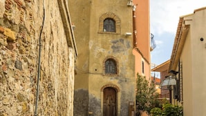Eine enge Kopfsteinpflasterstraße, gesäumt von historischen Steinbauten, wobei ein Gebäude in der Mitte eine Holztür und Rundbogenfenster besitzt.