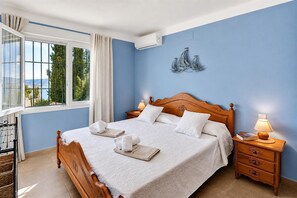 Een slaapkamer met een houten bed, twee bedlampen, een raam met gordijnen en een wandairconditioning.
