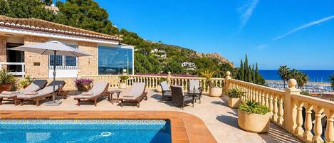 A poolside area with lounge chairs, a swimming pool, and a view of the sea.