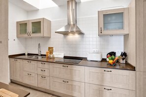Une cuisine moderne avec des meubles en bois clair, des appareils électroménagers en acier inoxydable et une hotte de cuisson centrale.