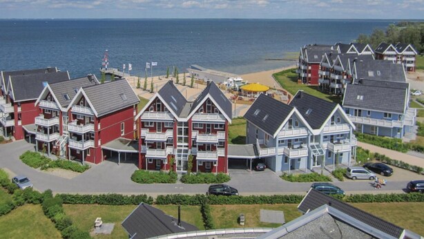 Un hôtel situé sur la côte, composé de plusieurs bâtiments à étages, offrant une vue sur la plage et disposant d’un parking.