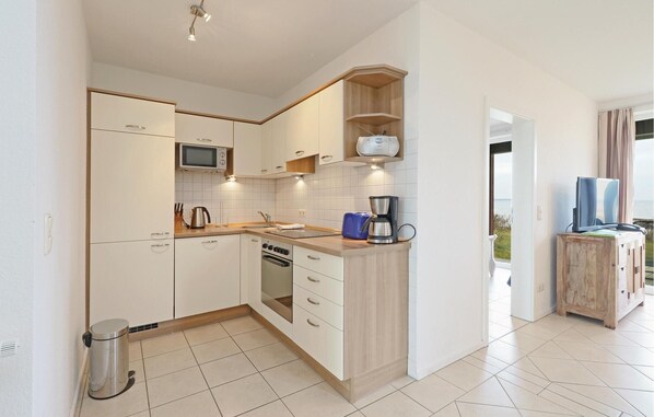 Una cocina moderna con armarios blancos, microondas, cafetera y tostadora. Hay un bote de basura y una ventana con vistas al exterior.
