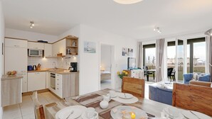 A modern kitchen with white cabinets, a microwave, and a coffee machine. There is a dining area with a table set for two, and a view of the outdoors through large windows. - 2 bedroom gorgeous apartment in Rechlin (Rechlin)