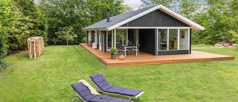 Une maison moderne dotée d’une terrasse, de deux chaises longues et d’une pelouse bien entretenue.