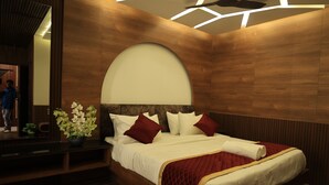 A modern hotel room with a wooden headboard, a large mirror, and a bed with white linens and red accents. - Ramana Towers (Tiruvannamalai)