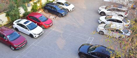 Un estacionamiento con varios autos, un edificio de fachada amarilla y blanca, y algo de vegetación.