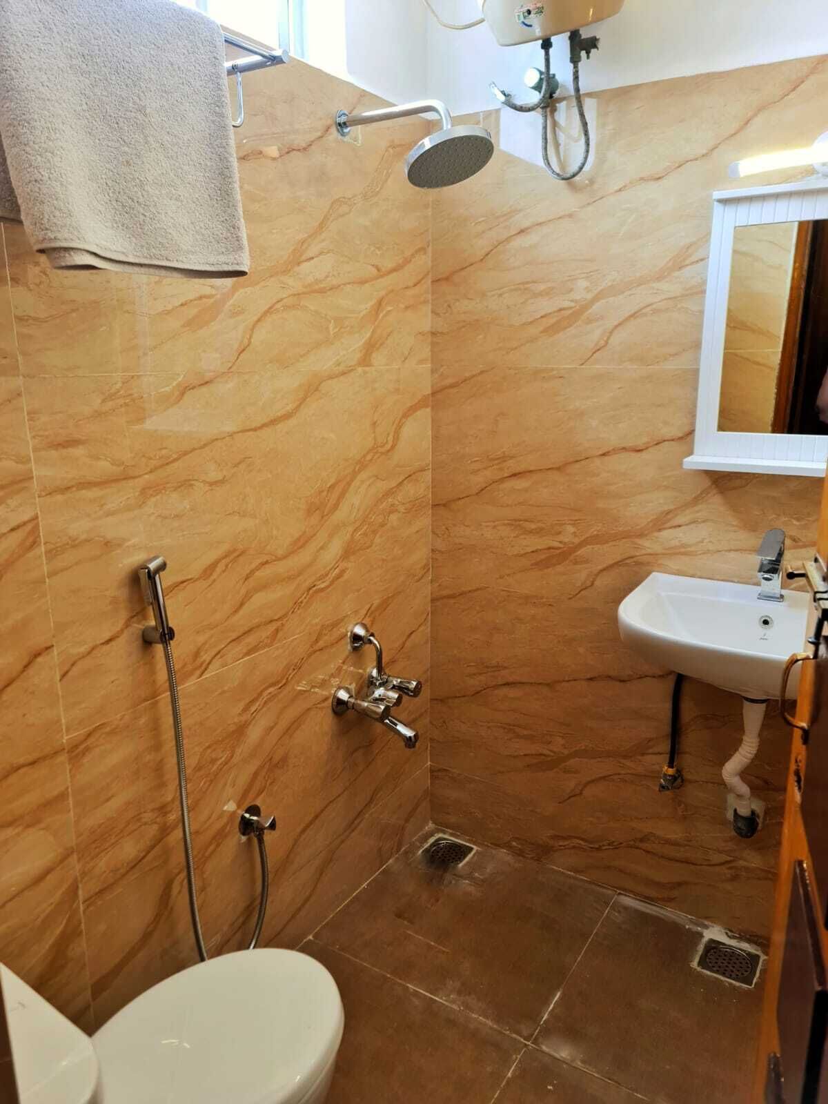 A bathroom with a marble wall, a shower, a toilet, and a sink.