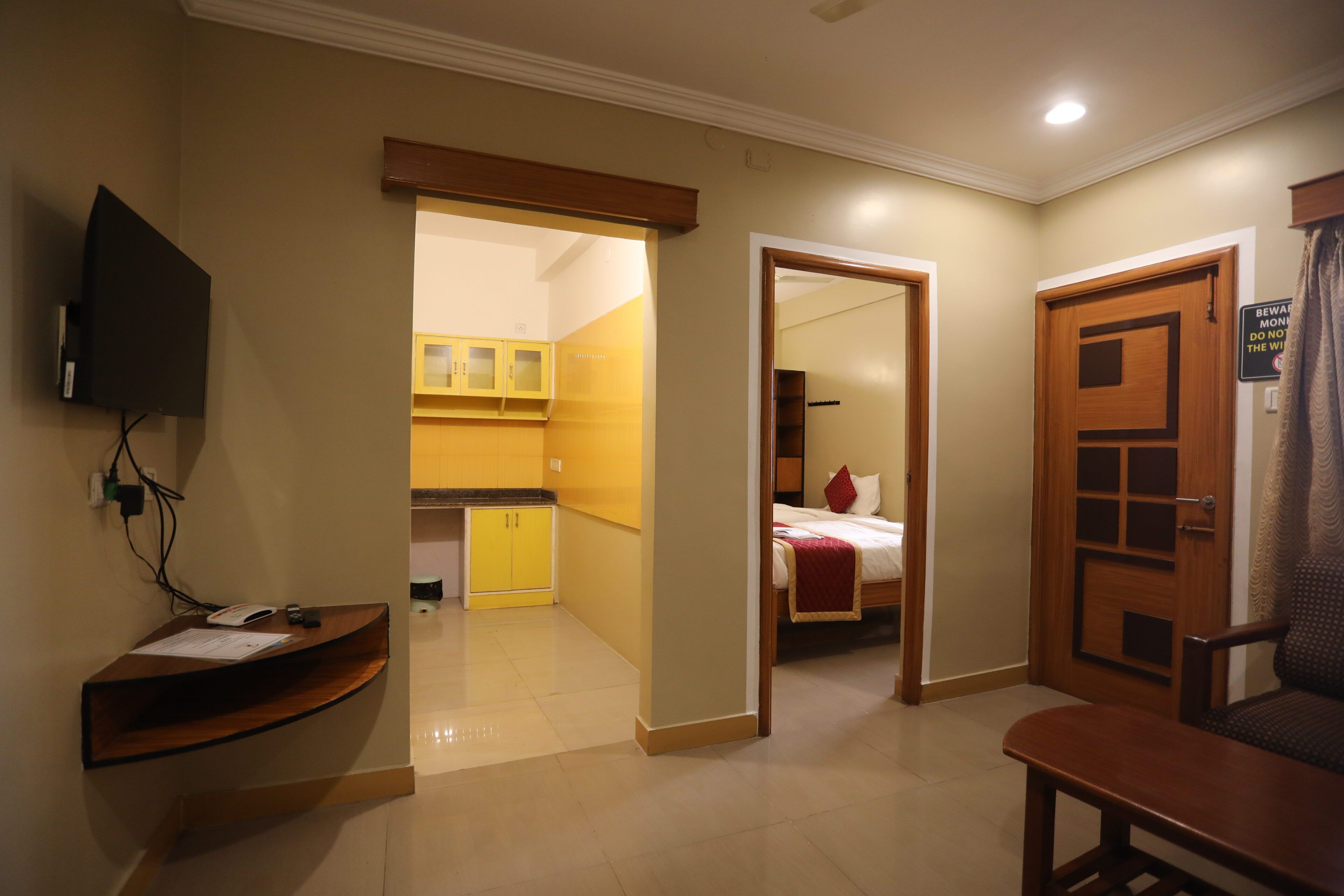A hotel room with a wooden desk, a bed with a red pillow, and a TV mounted on the wall.