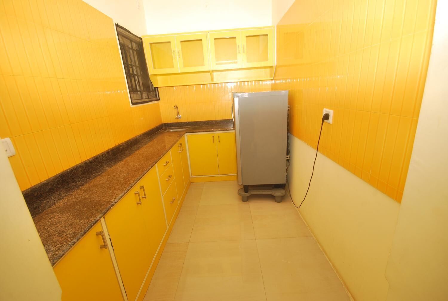 Una cocina compacta con gabinetes amarillos, una encimera de granito y un refrigerador plateado.