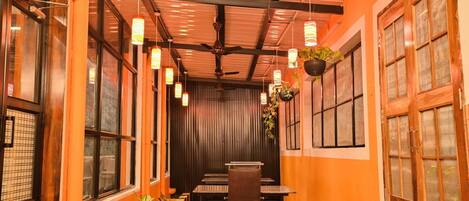 Un restaurante con un largo pasillo, mesas de madera, plantas colgantes y un ventilador de techo.