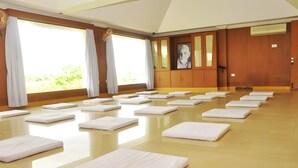 A spacious room with a polished floor, large windows with curtains, and multiple white mats arranged for activities. - Ramana Towers (Tiruvannamalai)