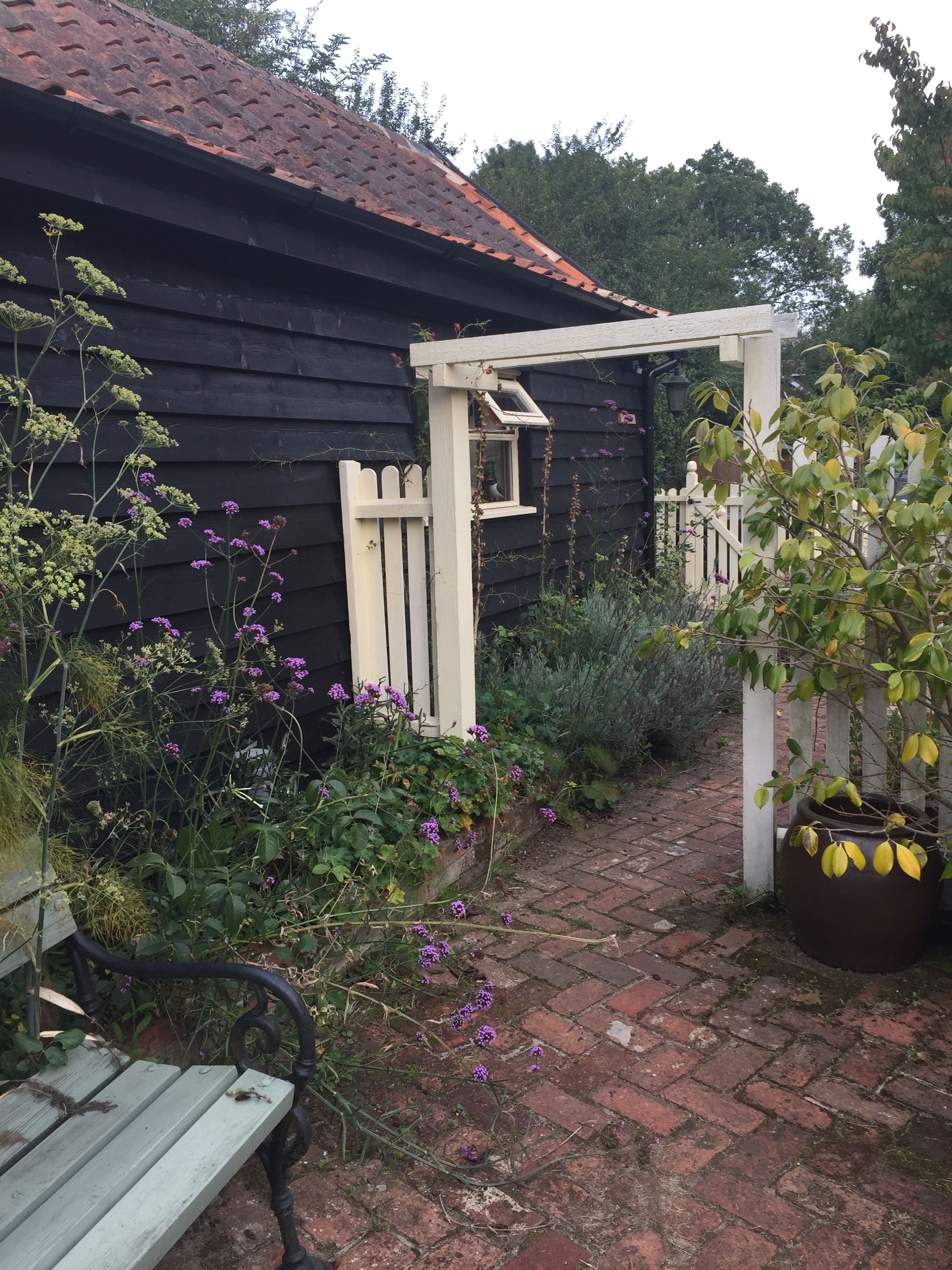 A garden pathway leading to a wooden house with a white picket fence and a wooden bench.