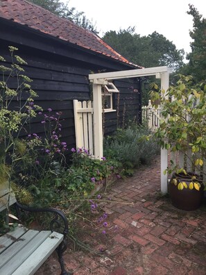 A garden pathway leading to a wooden house with a white picket fence and a wooden bench.