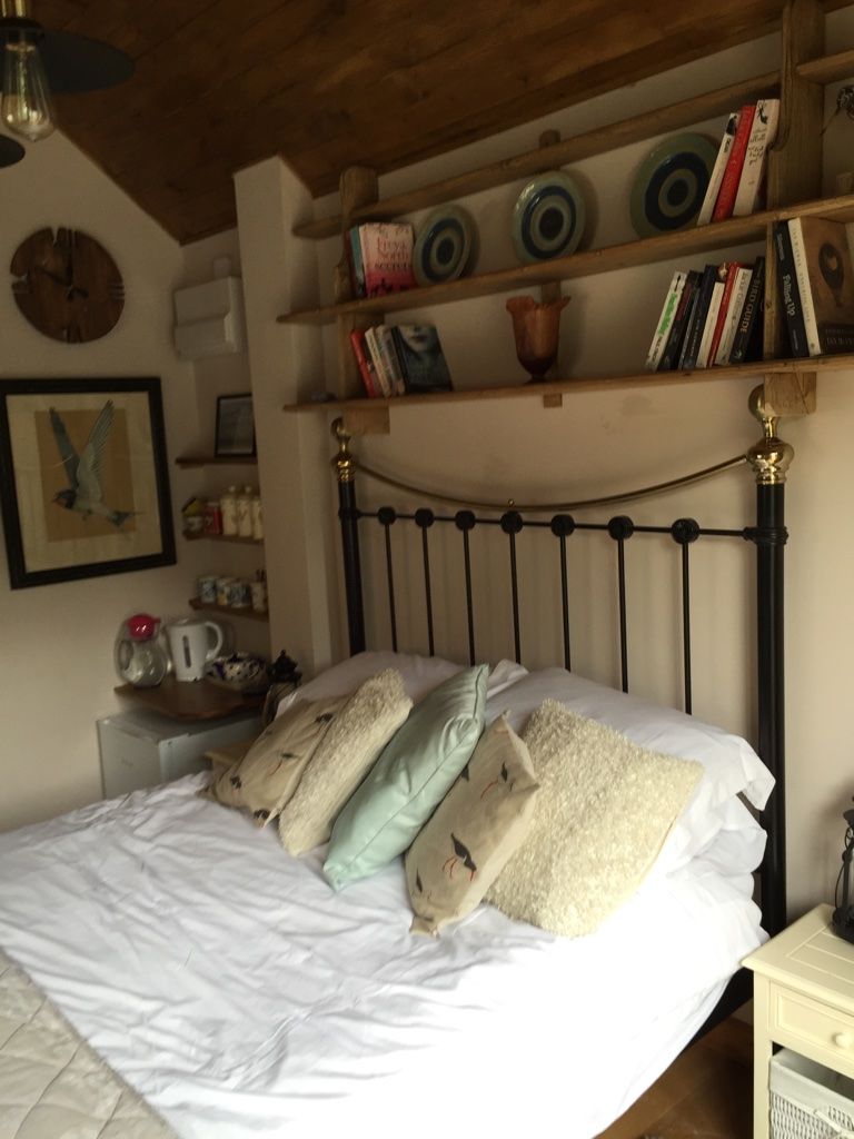 A bedroom with a bed, bedside table, and a shelf with books and decorative plates.