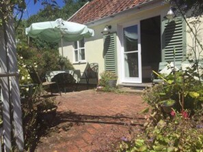 A house with a brick pathway leading to a door, surrounded by greenery and a white umbrella.