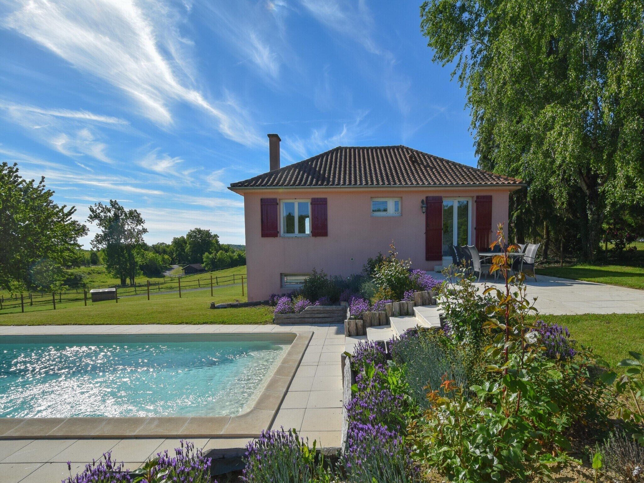 A house with a swimming pool, surrounded by a garden with various plants and flowers.
