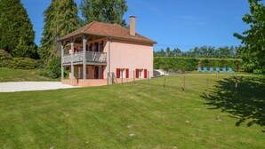 Une maison à deux étages dotée d’un balcon, entourée d’une pelouse bien entretenue et d’arbres.