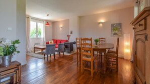 Un vaste espace de vie comprenant une table à manger en bois, des chaises et un canapé rouge. On y trouve également une cheminée, une fenêtre avec des rideaux et un tableau accroché au mur.