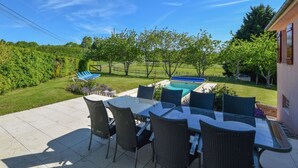 Un espace patio avec une table à plateau de verre et des chaises en osier, une piscine et une vue sur un paysage verdoyant.