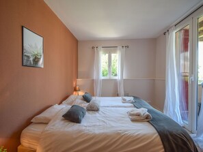Habitación de hotel con una cama grande, una mesita de noche con lámpara, una ventana con cortinas y vistas al exterior con vegetación.