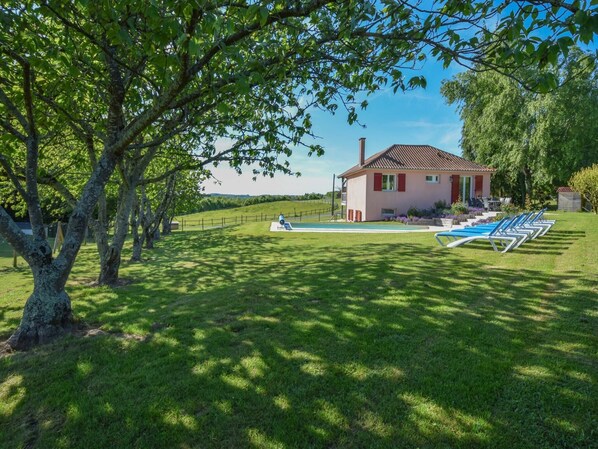 Una casa con piscina, rodeada de césped verde exuberante y árboles.