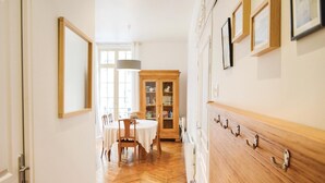 A hallway with a wooden floor, a dining area with a table and chairs, a cabinet with glass doors, and a wall with hooks.