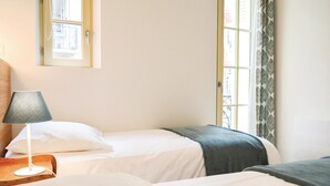 A hotel room with two beds, a lamp, and a window with patterned curtains.