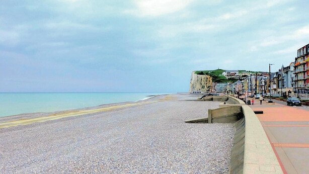 A pebble beach with a cliff and buildings in the background.