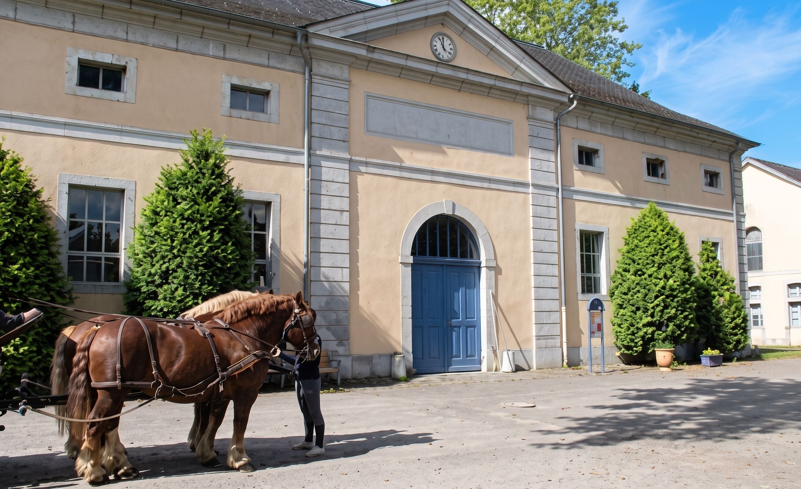 Un bâtiment avec une porte bleue, une horloge au-dessus, et deux chevaux devant.