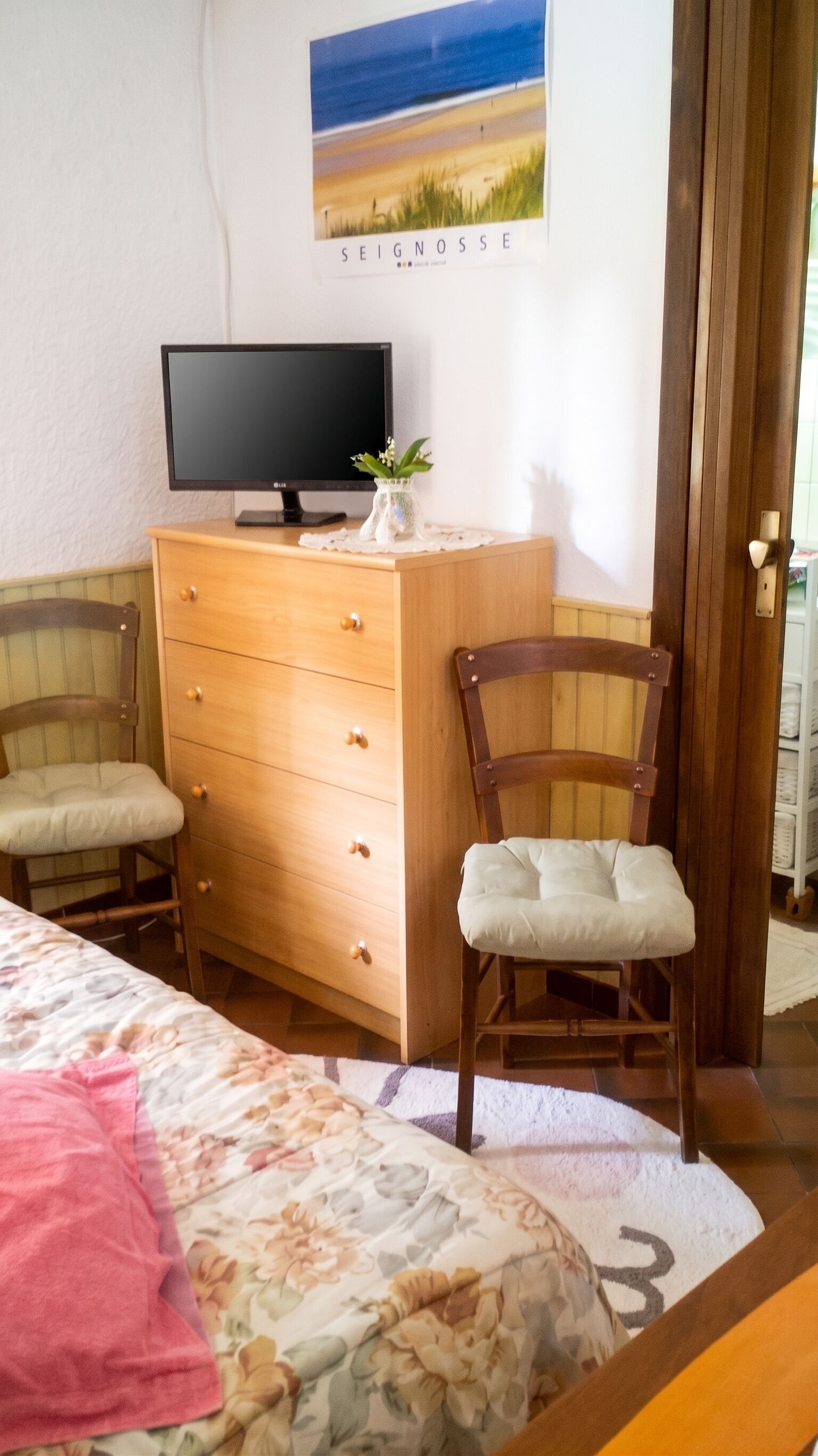 Ein Schlafzimmer mit einem Bett, einer Holzkommode, einem Fernseher und einem Sessel.