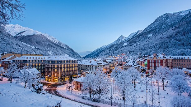 Une ville enneigée, avec des bâtiments, une route et des montagnes en arrière-plan.