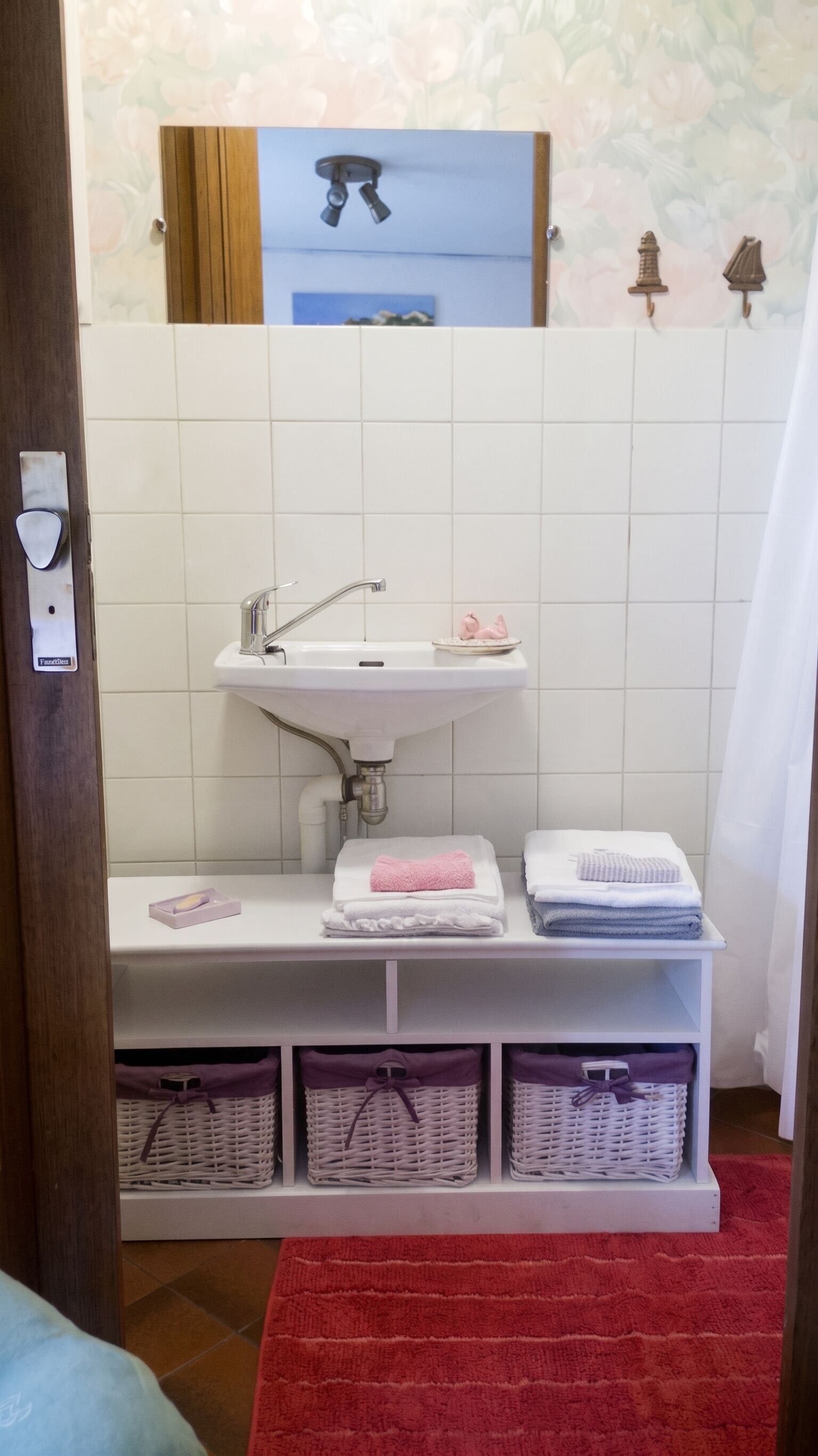 A bathroom with a white sink, a mirror, and a red towel on the floor.