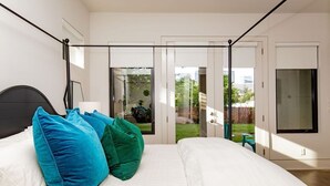 A bedroom with a bed, pillows, a nightstand, a window, and a sliding glass door leading to a balcony.