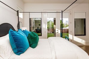 A bedroom with a bed, pillows, a nightstand, a window, and a sliding glass door leading to a balcony. - Designer Comforts, Concierge & Eco-Friendly Luxury (Austin)