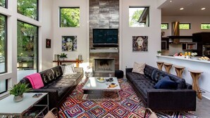A spacious living area with a fireplace, large windows, and a modern kitchen. - Designer Comforts, Concierge & Eco-Friendly Luxury (Austin)