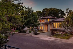 A modern two-story house with a metal roof, a front porch, and a driveway. - Designer Comforts, Concierge & Eco-Friendly Luxury (Austin)