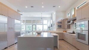 A modern kitchen with a central island, stainless steel appliances, and large windows. - Designer Comforts, Concierge & Eco-Friendly Luxury (Austin)