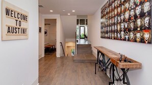 A hallway with a wooden bench, a 'WELCOME TO AUSTIN!' sign, and a wall of portraits.