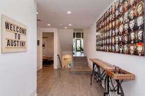 A hallway with a wooden bench, a 'WELCOME TO AUSTIN!' sign, and a wall of portraits. - Designer Comforts, Concierge & Eco-Friendly Luxury (Austin)