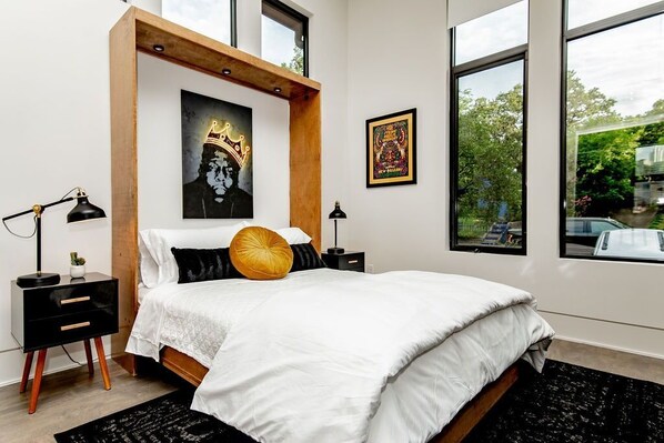 A bedroom with a bed, a nightstand, a lamp, and two framed pictures on the wall. - Designer Comforts, Concierge & Eco-Friendly Luxury (Austin)