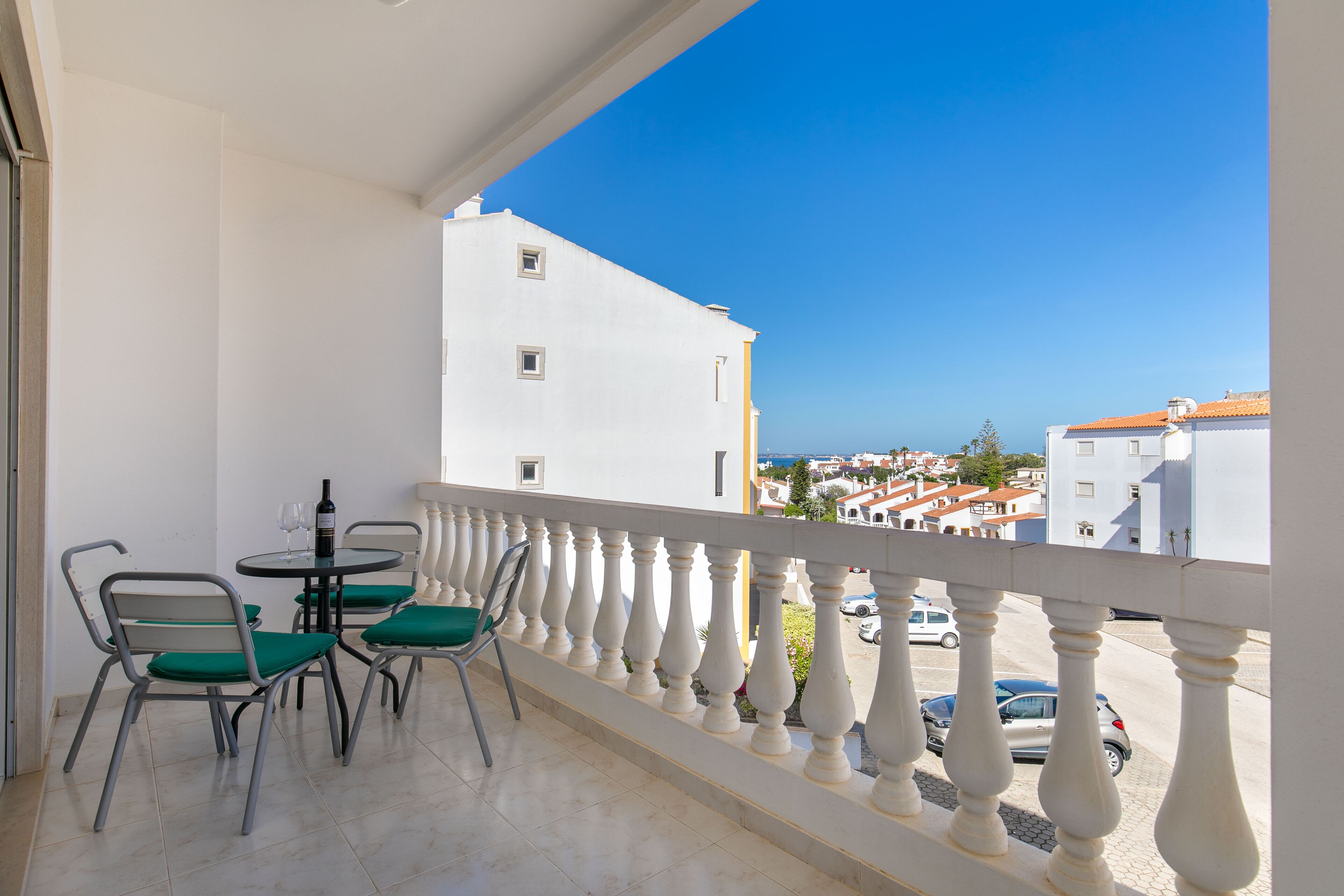 Un balcon doté d’une balustrade blanche, une table avec des chaises et une vue sur des bâtiments et des voitures au loin.