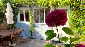 A wooden deck with a table and chairs, surrounded by lush greenery and a white building with windows. - House / Villa - La rochelle (La Rochelle)