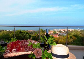 Un balcon avec une planche de charcuterie, une bouteille de vin et un chapeau de paille.