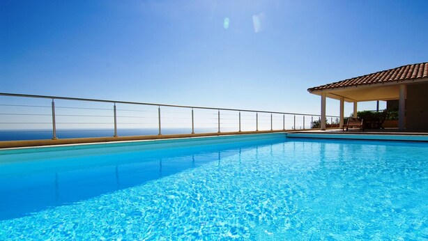 A clear blue pool with a view of the ocean, a covered seating area, and a railing along the pool's edge.